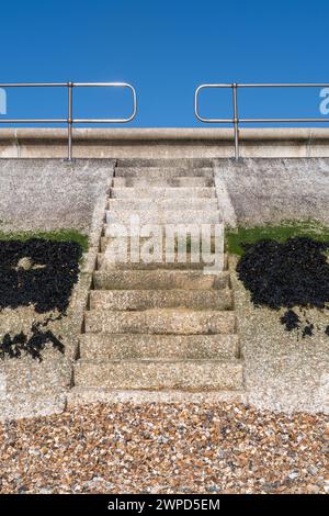 Stufen in der Meeresmauer, die vom Kiesstrand zur Straße bei Hill Head in der Nähe von Titchfield, Hampshire, England, Großbritannien, mit Algen und blauem Himmel führen Stockfoto