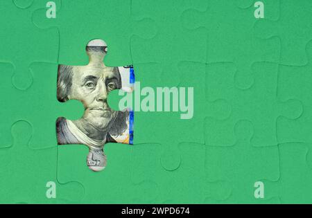 Grüner Puzzle-Hintergrund, der einige Teile von 100-Dollar-Scheinen enthüllt. Aufbau von Wohlstand durch harte Arbeit und Finanzplanung. Stockfoto