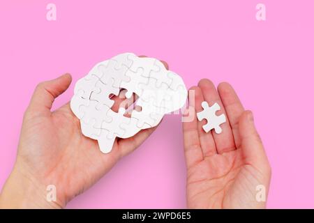 Weißes, hirnförmiges Puzzle in einer Hand und das fehlende Puzzleteil in der anderen. Reise zu psychischer Gesundheit und Wohlbefinden. Stockfoto