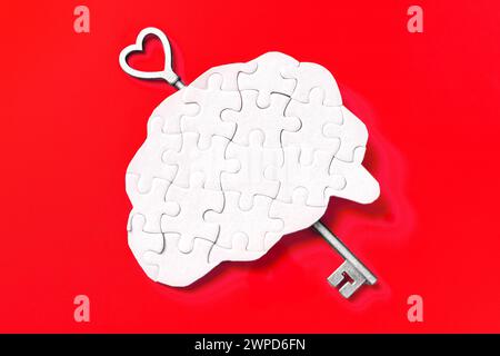 Menschliches, hirnförmiges Puzzle, gepaart mit einem Schlüssel, vor einem auffälligen roten Hintergrund. Geheimnisse des Geistes freischalten. Stockfoto