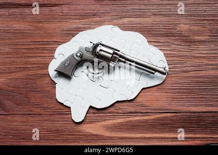 Revolver, der auf einem menschlichen Gehirn-förmigen Puzzle vor einer rustikalen Holzkulisse liegt. Kreativitäts- und Zerstörungskonzept. Stockfoto