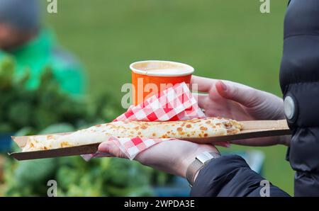 Mittelteil eines Kunden, Besucher des Bauernmarktes mit Papiertablett mit französischem Pfannkuchen, Krepp und einer Tasse Kaffee aus Papier, die ich Hände. Stockfoto
