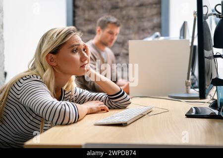 Junge Frau müde, erschöpft von der Arbeit. Gelangweilt und frustriert beim Blick auf den Computer. Stockfoto