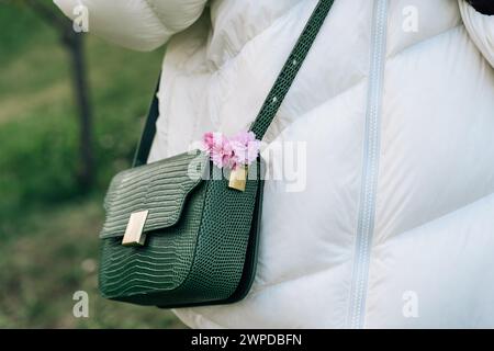 Modische modische Reptilienimitation Damenhandtaschen mit rosafarbenen japanischen Kirschblüten auf der Schulter der Frau während eines Spaziergangs im Frühlingsgarten Stockfoto