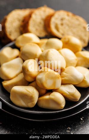 Geräucherter Mini-Scamorza-Käse. Traditioneller italienischer Käse auf Teller auf dem schwarzen Tisch. Stockfoto