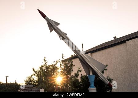 Ein Modelljet fliegt bei Sonnenlicht an einem Gebäude in der Nähe von Bäumen vorbei Stockfoto