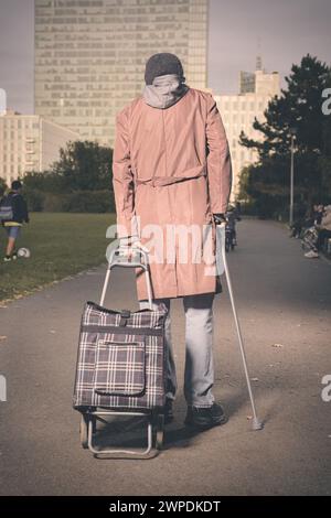 Seniorin zu Fuß mit Rollwagen und Stock im Stadtpark Stockfoto