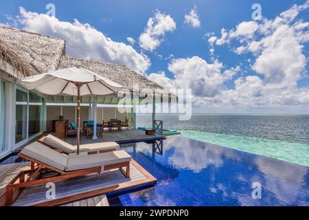 Luxuriöses Strandresort, Bungalow in der Nähe des endlosen Pools über dem wunderschönen blauen Meer. Fantastische tropische Insel, Sommerurlaubskonzept. Ein paar Stühle mit Sonnenschirm Stockfoto