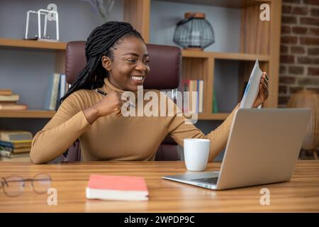 Fröhliche Frau mit Dreadlocks arbeitet ferngesteuert mit Laptop und Technologie Stockfoto