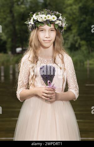 Nette junge Dame posiert im Teichwasser in Kleidung mit Lavendelstrauß Stockfoto