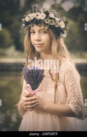 Nette junge Dame posiert im Teichwasser in Kleidung mit Lavendelstrauß Stockfoto