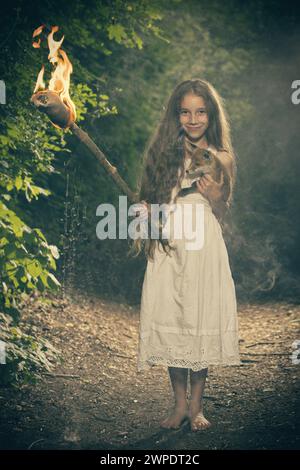 Nette junge Dame posiert im dunklen Wald in Kleidung mit Fackel in Flammen Stockfoto