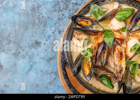 Eintopf mit Meeresfrüchten in Keramikschale mit Blick von oben. Garnelen, Muscheln und Calamari-Ringe in cremiger Sauce mit Knoblauch, Sellerie, Zwiebeln und frischer Petersilie. Nahaufnahme. Cop Stockfoto