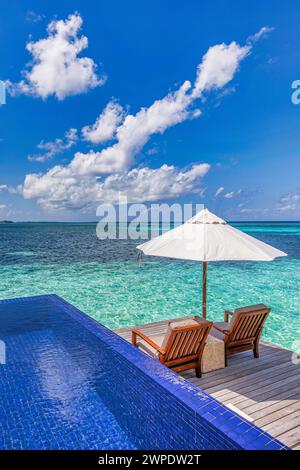 Luxuriöses Strandresort, Bungalow in der Nähe des endlosen Pools über dem wunderschönen blauen Meer. Fantastische tropische Insel, Sommerurlaubskonzept. Ein paar Stühle mit Sonnenschirm Stockfoto