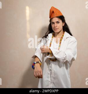 Eine selbstbewusste junge Frau in einem knusprigen weißen Hemd und einem traditionellen afrikanischen Hut steht mit farbenfrohen Perlen, die eine Mischung aus modernem Stil verkörpern Stockfoto