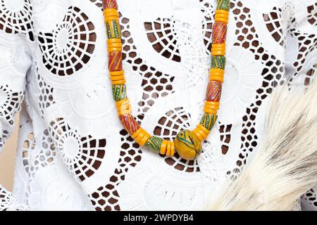 Eine detaillierte Nahaufnahme, die das komplizierte Design einer traditionellen afrikanischen Halskette auf einem bestickten weißen Kleidungsstück unterstreicht Stockfoto