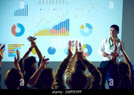 Geschäftsschulung, umgeben von Datenvisualisierungen, bei denen der Mann die Rede beendet und das Publikum klatscht, die Hände zu heben. Stockfoto