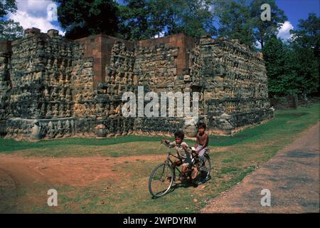 Jungen auf dem Fahrrad an der Wand der Terrasse mit Schnitzereien, Elefantenterrasse, Angkor Thom, Angkor Wat Komplex, Siem Riep, Kambodscha Stockfoto