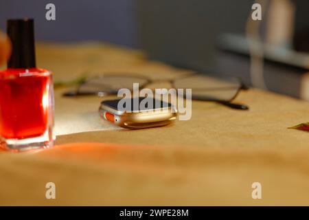 Diese Ansicht zeigt eine elegante Smart-Uhr, nagellack und Sonnenglas. In der Tabelle brauner Hintergrund. Lichtreflexion Stockfoto