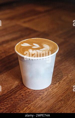 Nahaufnahme einer Tasse zum Mitnehmen mit herzförmiger Latte Art auf Holztafel Stockfoto