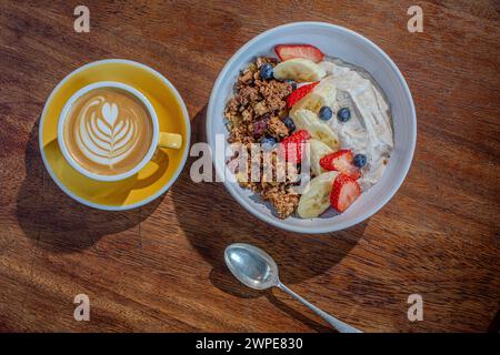 Eine Tasse flacher weißer Kaffee mit einer Schüssel Müsli und Joghurt auf dem Holztisch im Café. Stockfoto
