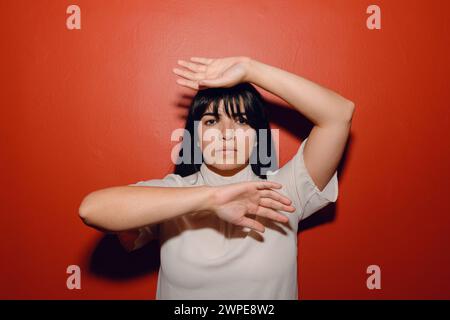 Porträt einer jungen lateinischen Frau, verzweifelt, verängstigt, mit den Händen davor, die auf rotem Hintergrund stehen, ernsthafte Gesten mit Gesicht und Händen machen. Stockfoto