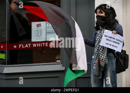 Ein Demonstrant steht vor Pret A Krippe mit einer palästinensischen Flagge und einem Plakat mit der Aufschrift "diese Kompanie unterstützt den israelischen Völkermord, tritt dem Boykott bei" während einer Demonstration. Demonstranten fordern, dass die Leute Costa Coffee boykottieren. Ihre Muttergesellschaft Coca-Cola betreibt eine Fabrik in der illegalen israelischen Siedlung Atarot in dem Gebiet, das von den Demonstranten als Palästina besetzt angesehen wird. Die Boykott Divestment and Sanctions (BDS)-Bewegung arbeitet daran, die internationale Unterstützung für Israels Unterdrückung der Palästinenser zu beenden und Israel unter Druck zu setzen, sich an das Völkerrecht zu halten, und hat eine Liste von Unternehmen zusammengestellt Stockfoto