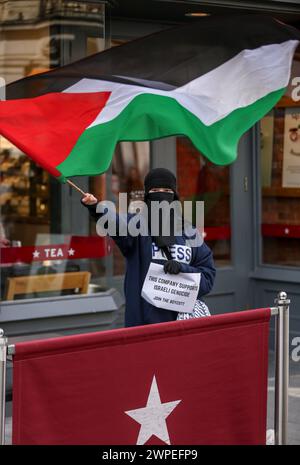 Ein Demonstrant steht vor Pret A Krippe mit einer palästinensischen Flagge und einem Plakat mit der Aufschrift "diese Kompanie unterstützt den israelischen Völkermord, tritt dem Boykott bei" während einer Demonstration. Demonstranten fordern, dass die Leute Costa Coffee boykottieren. Ihre Muttergesellschaft Coca-Cola betreibt eine Fabrik in der illegalen israelischen Siedlung Atarot in dem Gebiet, das von den Demonstranten als Palästina besetzt angesehen wird. Die Boykott Divestment and Sanctions (BDS)-Bewegung arbeitet daran, die internationale Unterstützung für Israels Unterdrückung der Palästinenser zu beenden und Israel unter Druck zu setzen, sich an das Völkerrecht zu halten, und hat eine Liste von Unternehmen zusammengestellt Stockfoto