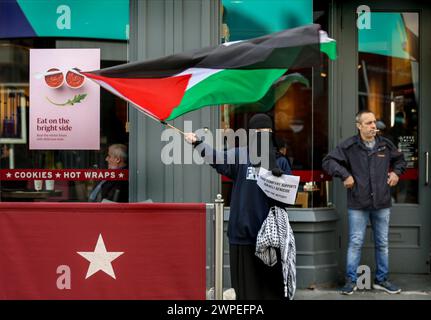 Ein Demonstrant steht vor Pret A Krippe mit einer palästinensischen Flagge und einem Plakat mit der Aufschrift "diese Kompanie unterstützt den israelischen Völkermord, tritt dem Boykott bei" während einer Demonstration. Demonstranten fordern, dass die Leute Costa Coffee boykottieren. Ihre Muttergesellschaft Coca-Cola betreibt eine Fabrik in der illegalen israelischen Siedlung Atarot in dem Gebiet, das von den Demonstranten als Palästina besetzt angesehen wird. Die Boykott Divestment and Sanctions (BDS)-Bewegung arbeitet daran, die internationale Unterstützung für Israels Unterdrückung der Palästinenser zu beenden und Israel unter Druck zu setzen, sich an das Völkerrecht zu halten, und hat eine Liste von Unternehmen zusammengestellt Stockfoto