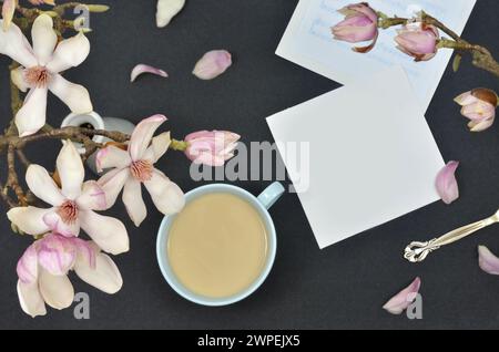 Magnolienblüten und weißes Blatt Papier zum Füllen, Kaffee mit Milch, Noten, dunkler Hintergrund, flache Lagen. Stockfoto
