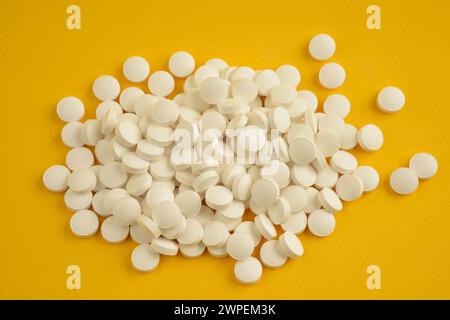 Nahaufnahme von oben eines Stapels weißer, runder Vitamin-D-Tabletten, der lose auf gelbem Hintergrund liegt Stockfoto