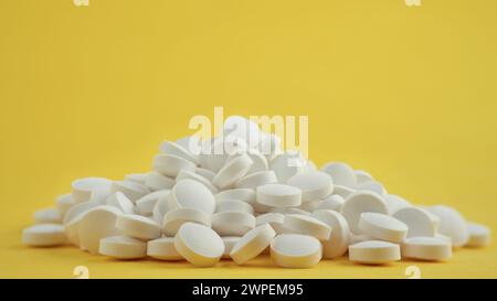 Nahaufnahme eines Stapels weißer, runder Vitamintabletten auf gelbem Hintergrund Stockfoto