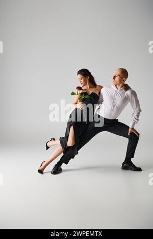 Elegante Tanzbewegung eines jungen brünetten Paares, einer Frau mit roter Rose und einem Mann, der im Studio auftritt Stockfoto