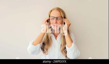 Erschöpfte, müde kaukasische Angestellte mittleren Alters mit Kopfschmerzen oder Schläfenschmerzen, leidet an Migräne, Verspannungen im Kopf zu Hause Stockfoto