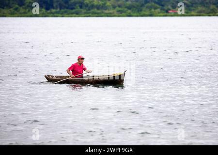 Ein einheimischer Mann in einem handgefertigten Kanu paddelt auf einem ruhigen Wasser in einer Bucht der Insel San Cristobal im Bocas del Toro Archipel am frühen Morgen, Panama Stockfoto