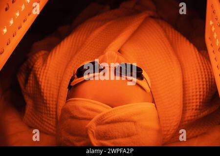 Eine ältere Frau durchläuft eine Gesichtsverjüngung. Frau Gesicht lt Rotlichtbehandlung in der Schönheitsklinik. Kosmetologie. Stockfoto