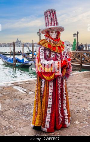 Eine Person, die für den Karneval gekleidet ist, vor den Gondeln und der Lagune von Venedig in Veneto, Italien Stockfoto