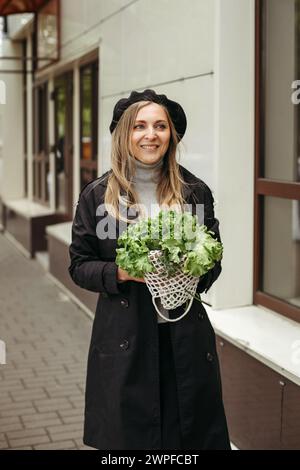 Eine Frau, die steht und einen Haufen Salat vor ihrem Gesicht hält. Vertikales Bild. Stockfoto