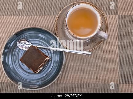 Tasse Tee mit köstlichem Kuchen. Komposition mit Tiramisu-Kuchen und Tee auf dem Tisch, Blick von oben. Tasse Tee mit Schokoladenkuchen Stockfoto