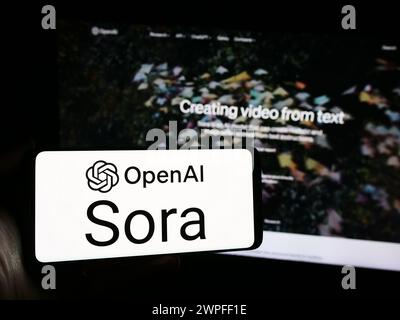 Person mit Smartphone und Logo der Text-to-Video-Modellsoftware Sora (OpenAI) vor der Website. Schwerpunkt auf dem Display des Telefons. Stockfoto