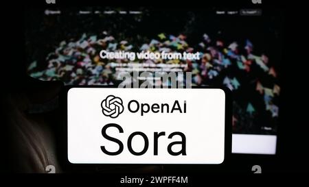 Person, die ein Mobiltelefon mit dem Logo der Text-to-Video-Modellsoftware Sora (OpenAI) vor der Unternehmenswebseite hält. Schwerpunkt auf dem Display des Telefons. Stockfoto