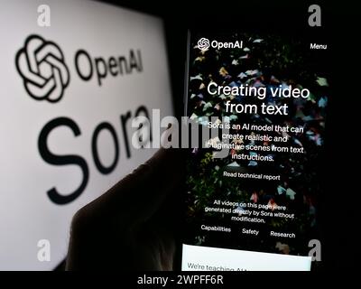 Person, die ein Mobiltelefon hält und vor dem Logo eine Webseite der Text-to-Video-Modellsoftware Sora (OpenAI) zeigt. Konzentrieren Sie sich auf die Mitte des Telefondisplays. Stockfoto