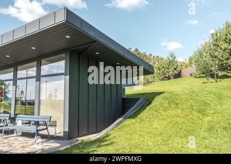 Modernes Gästehaus mit stehender Nahtfassade, Panoramaverglasung und großem Flachdach-Überhang im Park. Minimalistischer architektonischer Stil des öffentlichen Gebäudes Stockfoto