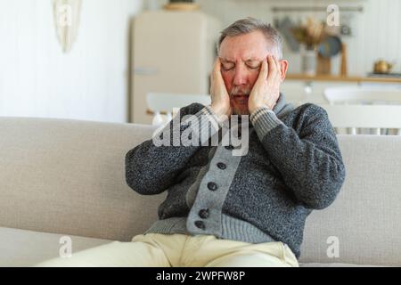 Kopfschmerz. Unglücklicher Mann mittleren Alters mit Kopfschmerz-kranken Reibungstempeln zu Hause. Reifer alter Großvater berührt Tempel unter Stress. Ein Mann, der Schmerzen im Kopf hat Stockfoto