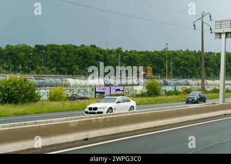 Lyon, Frankreich - 7. Mai 2023: Ein weißes Auto fährt auf einer Autobahn mit einem bunten Güterzug vor einem bewölkten Himmel. Stockfoto