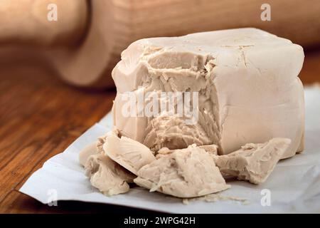 Zerknitterter Block frischer Hefe auf einem Holzbrett vor einer Nudelnadel, eine wichtige Zutat zum Backen von Brot oder Pizza Stockfoto