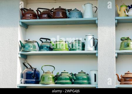 Eine Sammlung von Vintage-Wasserkocher, die auf einem Regal vor einer weißen Wand präsentiert werden. Das Array bietet eine Vielzahl von Farben und Oberflächen, die verschiedene Designzeiträume widerspiegeln. Stockfoto