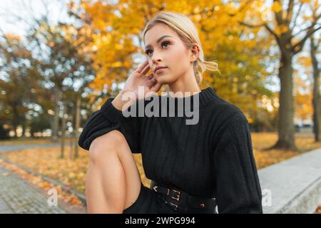 Frisches, schönes Herbstmädchen in Einem modischen schwarzen Strickpullover sitzt in einem Herbstpark mit gelbem Laub Stockfoto