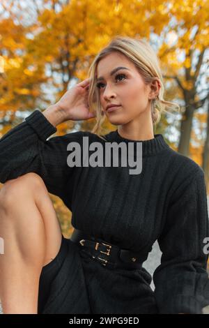 Das schöne frische junge Mädchen in Mode Schwarzes Strickkleid sitzt in einem Herbstpark mit goldenem Laub Stockfoto