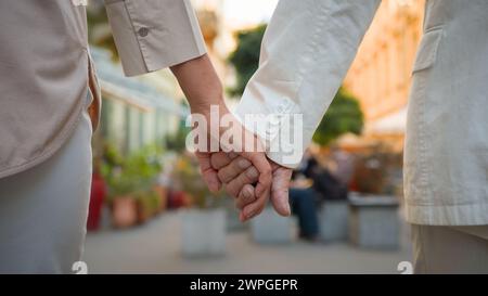 Nahaufnahme aus der Ferne eines nicht wiedererkennbaren romantischen älteren Ehepaares Ehemann, der Hände hält, während er zusammen außerhalb der Stadtstraße spaziert. Glück Stockfoto